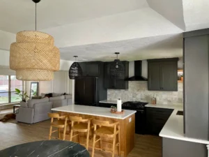 Open-concept kitchen featuring dark gray cabinets, a wood island, marble-look backsplash, and rattan pendant lights
