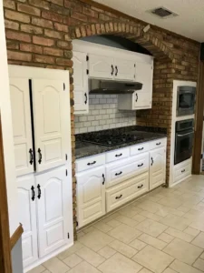 Rustic kitchen area with white cabinets, black granite countertops, subway tile, and an exposed brick archway